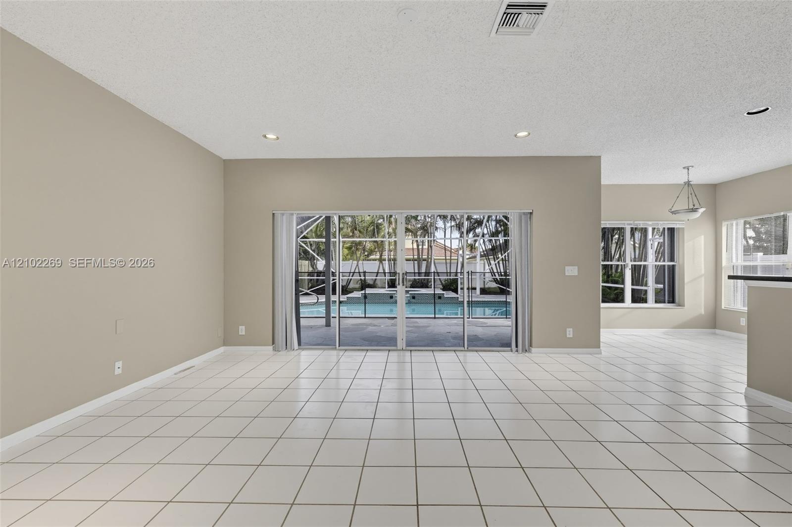 Open-concept space featuring large-format ceramic tile flooring, recessed lighting, and expansive glass sliding doors providing visibility to a screened-in pool and spa area