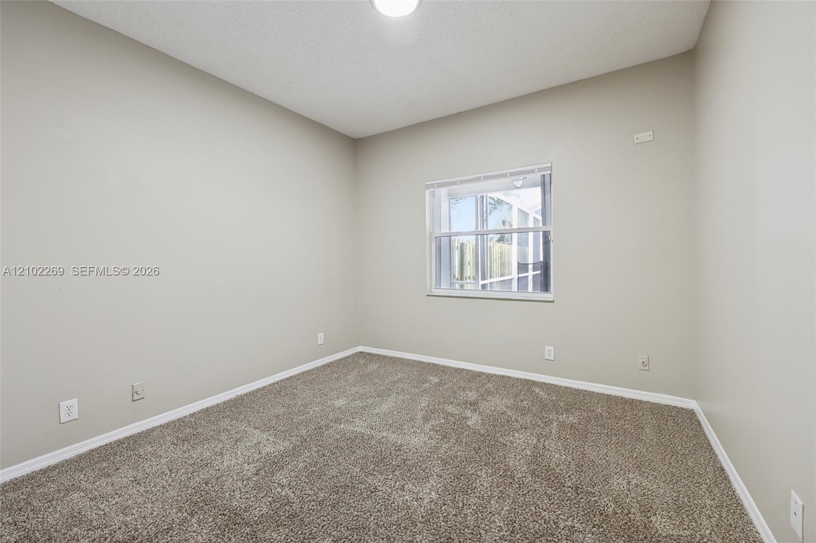 Neutral-toned interior space featuring neutral wall-to-wall carpeting, a single-pane window with white horizontal blinds, and overhead lighting
