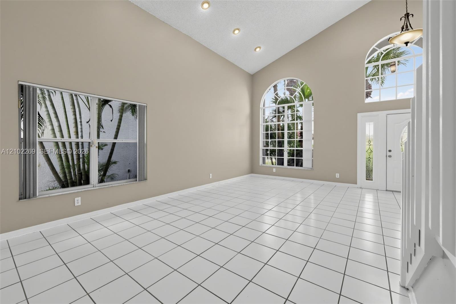 Vaulted ceilings, large arched windows, ceramic tile flooring, recessed lighting, and a front entry door with glass sidelights