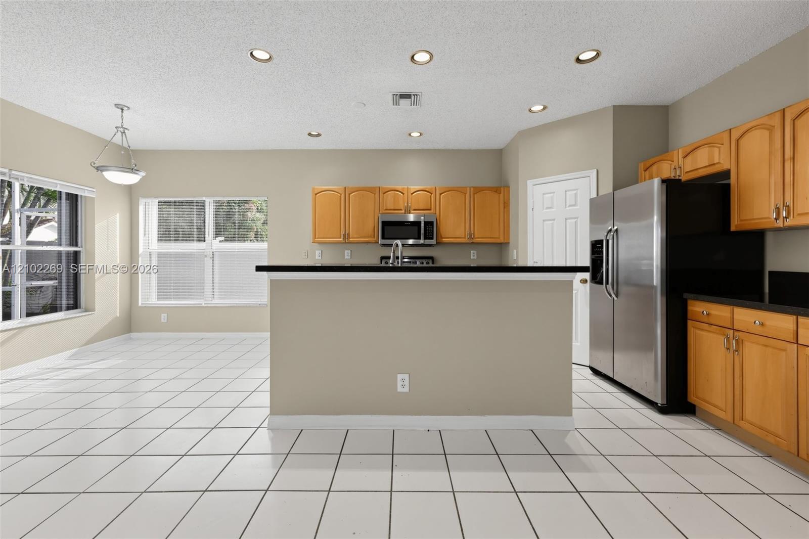 Kitchen featuring wood cabinetry, dark countertops, tile flooring, recessed lighting, and stainless steel refrigerator Kitchen featuring wood cabinetry, dark countertops, tile flooring, recessed lighting, and stainless steel refrigerator