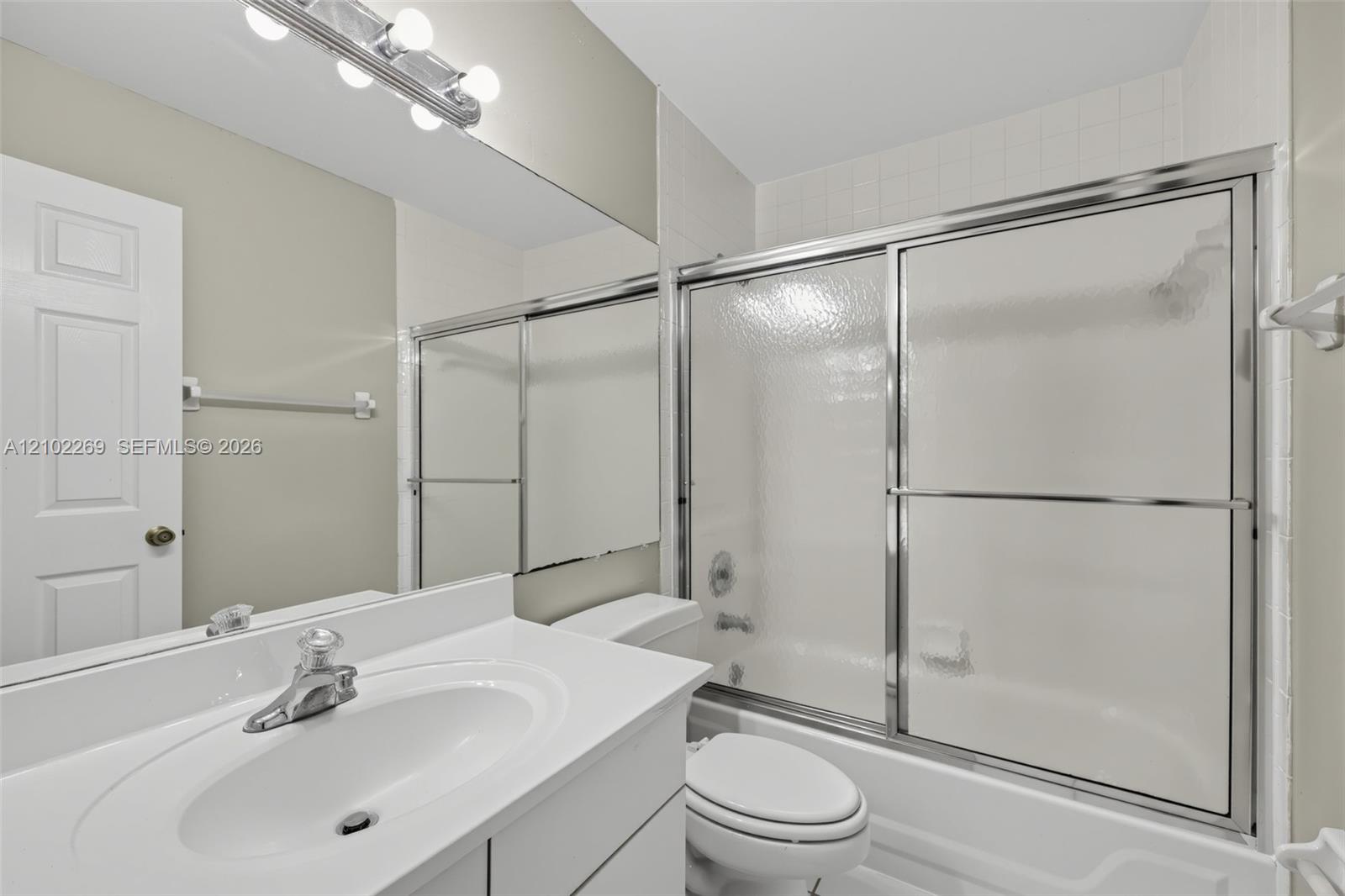 Bathroom featuring a white vanity with an integrated sink, a full-width vanity mirror, a multi-bulb light fixture, and a tub-shower combination with sliding glass doors