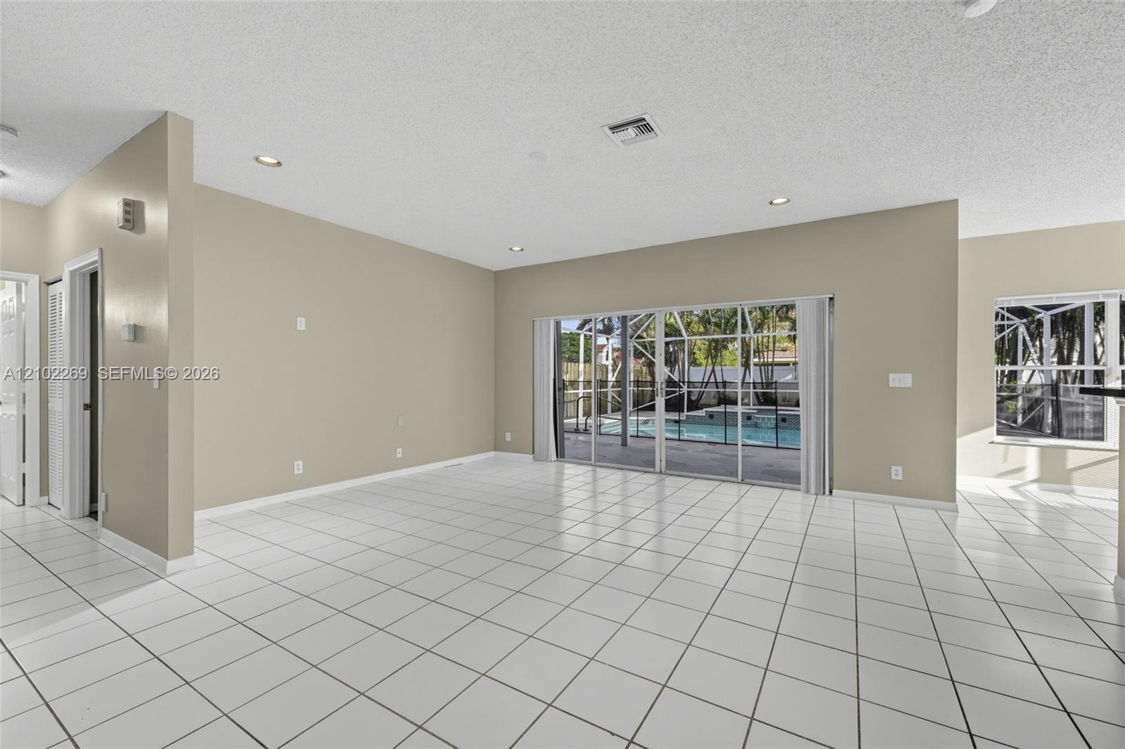 Neutral-toned interior featuring ceramic tile flooring, recessed lighting, and large sliding glass doors providing visibility to a screened-in pool area