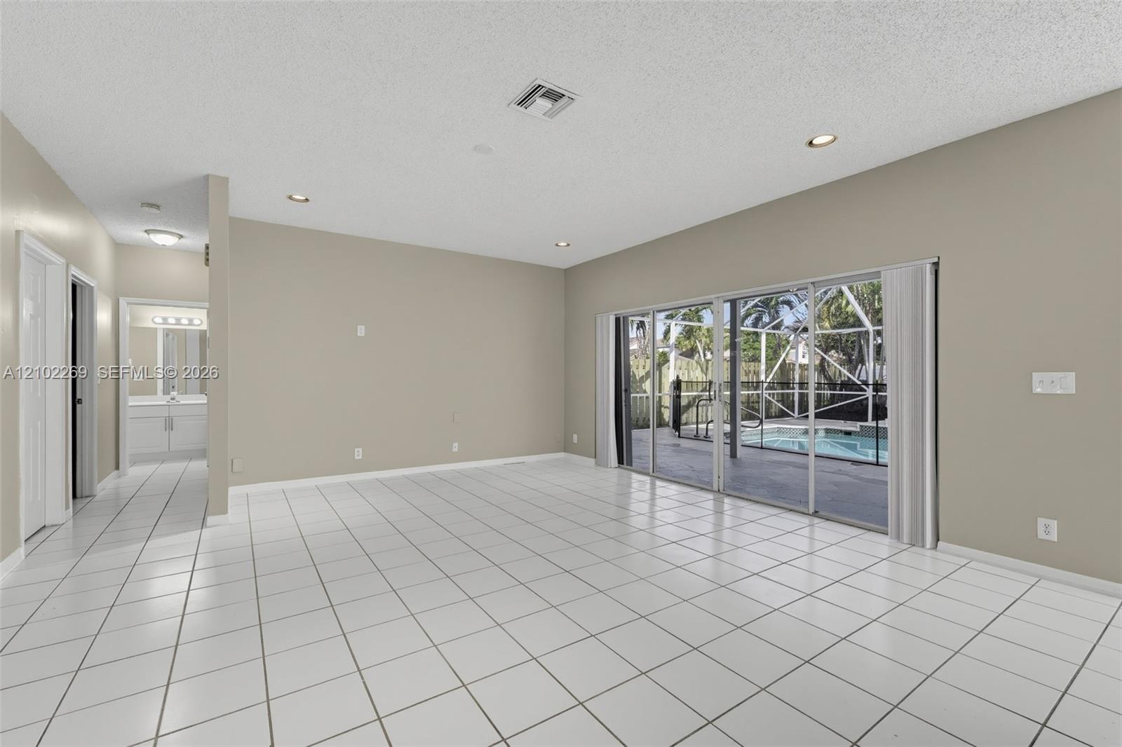 Open-concept interior featuring large-format tile flooring, recessed ceiling lighting, and expansive glass sliding doors providing visibility to a screened-in lanai with a pool