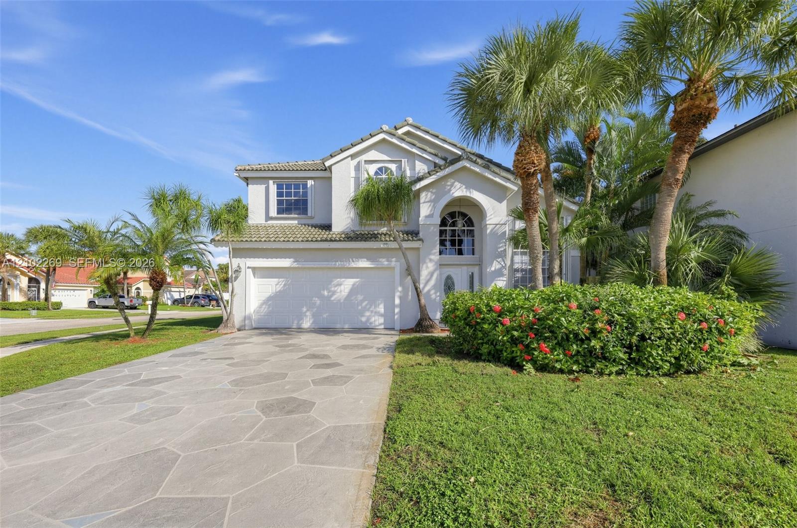 Two-story stucco exterior featuring a tiled roof, arched entryway, polygon-patterned paver driveway, and established palm landscaping Two-story stucco exterior featuring a tiled roof, arched entryway, polygon-patterned paver driveway, and established palm landscaping