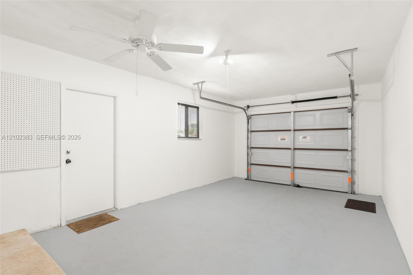 Enclosed garage featuring a multi-panel overhead door, finished concrete flooring, a ceiling-mounted fan, and integrated wall-mounted pegboard storage