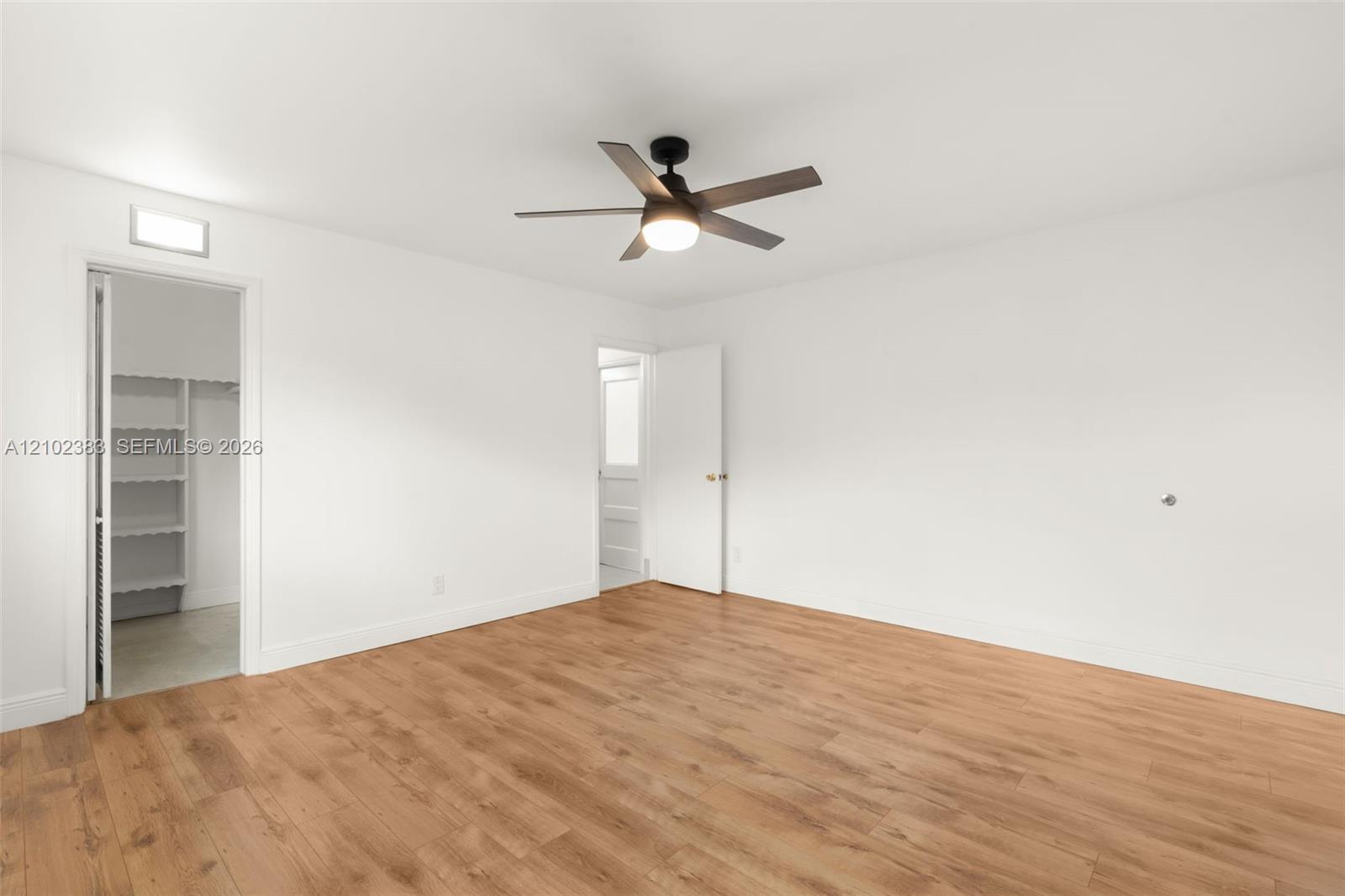 Primary bedroom Wood-finish flooring, multi-blade ceiling fan with integrated light, and walk-in closet with built-in shelving