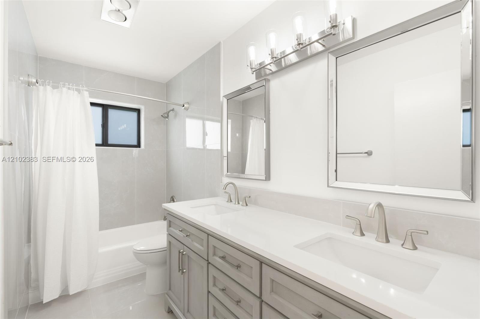 Bathroom featuring a dual-sink vanity with a solid-surface countertop, rectangular undermount basins, brushed nickel hardware, and two framed wall mirrors