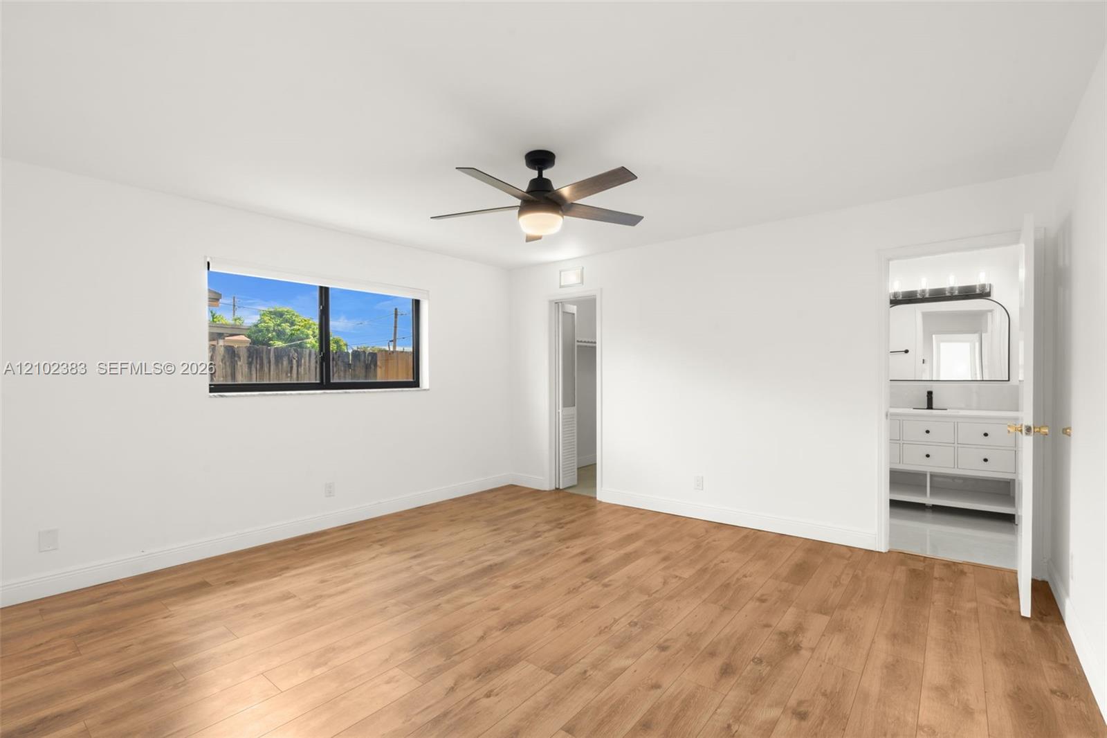 Primary bedroom featuring wood-finish flooring, a matte black ceiling fan with integrated lighting, and a single-pane window