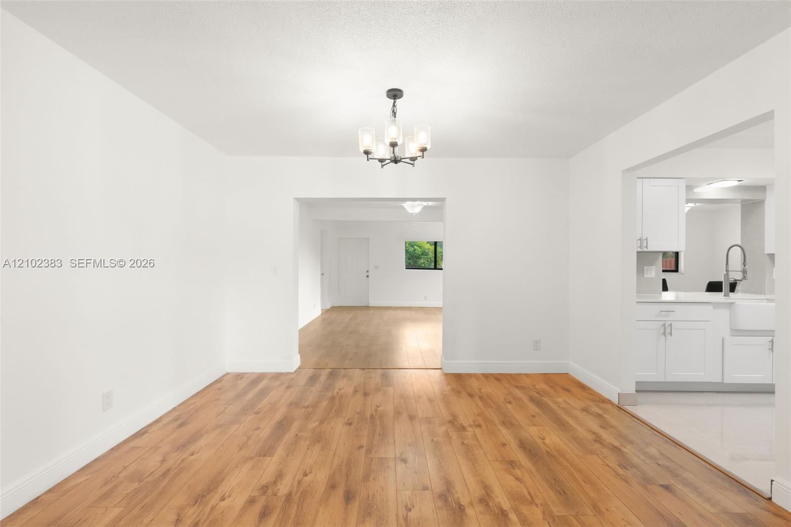 Dining area featuring wood-finish flooring, a contemporary multi-light chandelier, and white cabinetry with a farmhouse-style sink Dining area featuring wood-finish flooring, a contemporary multi-light chandelier, and white cabinetry with a farmhouse-style sink