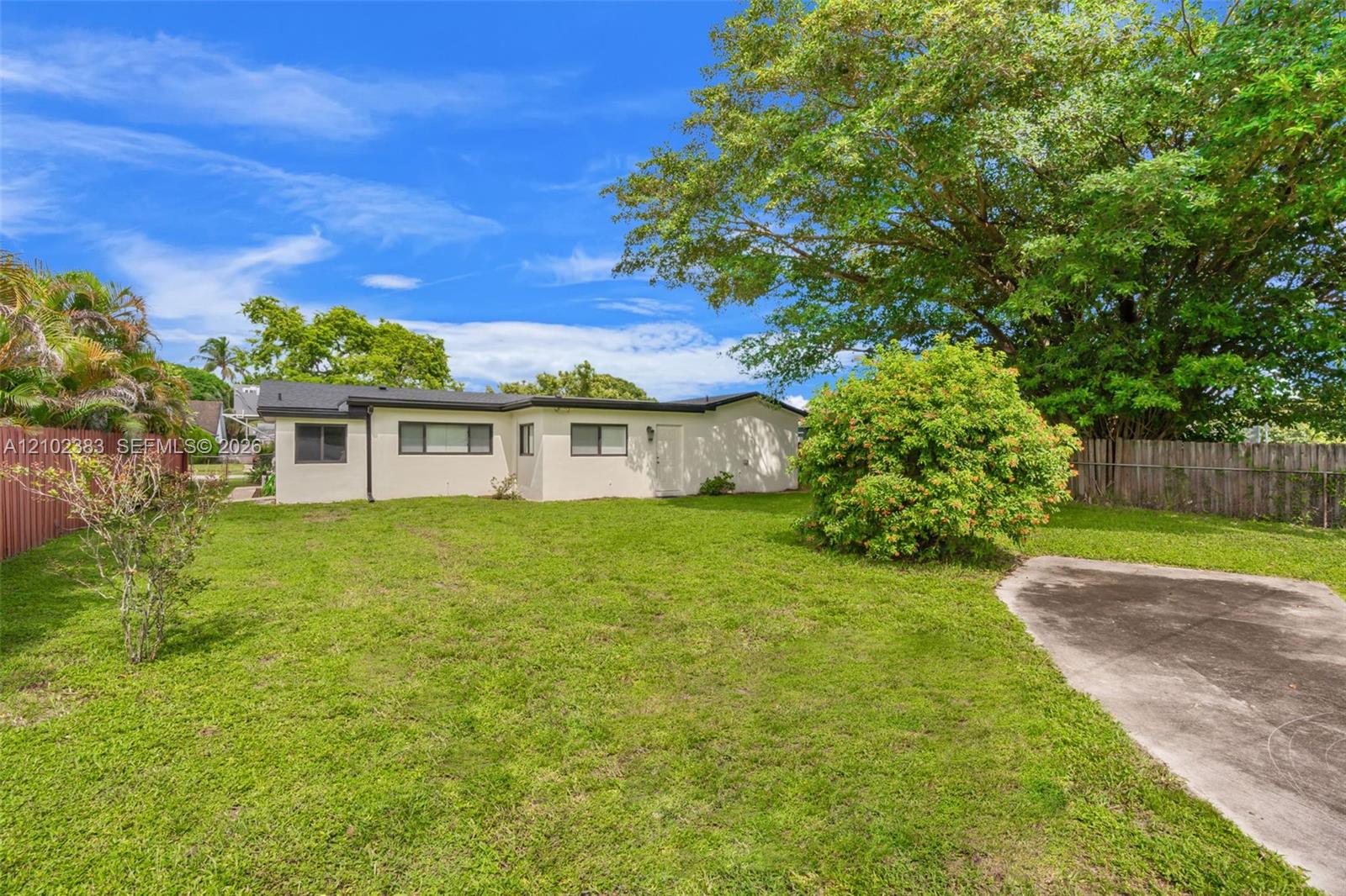 Expansive backyard featuring a grass lawn, mature trees, concrete hardscaping, and perimeter fencing