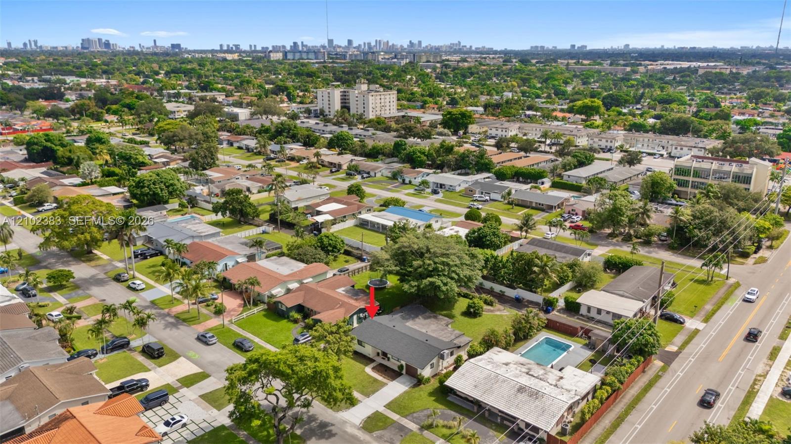 Aerial perspective of a residential property featuring a low-pitch roof, a multi-car concrete driveway, a front lawn with mature landscaping, and a rectangular swimming pool within a fenced backyard