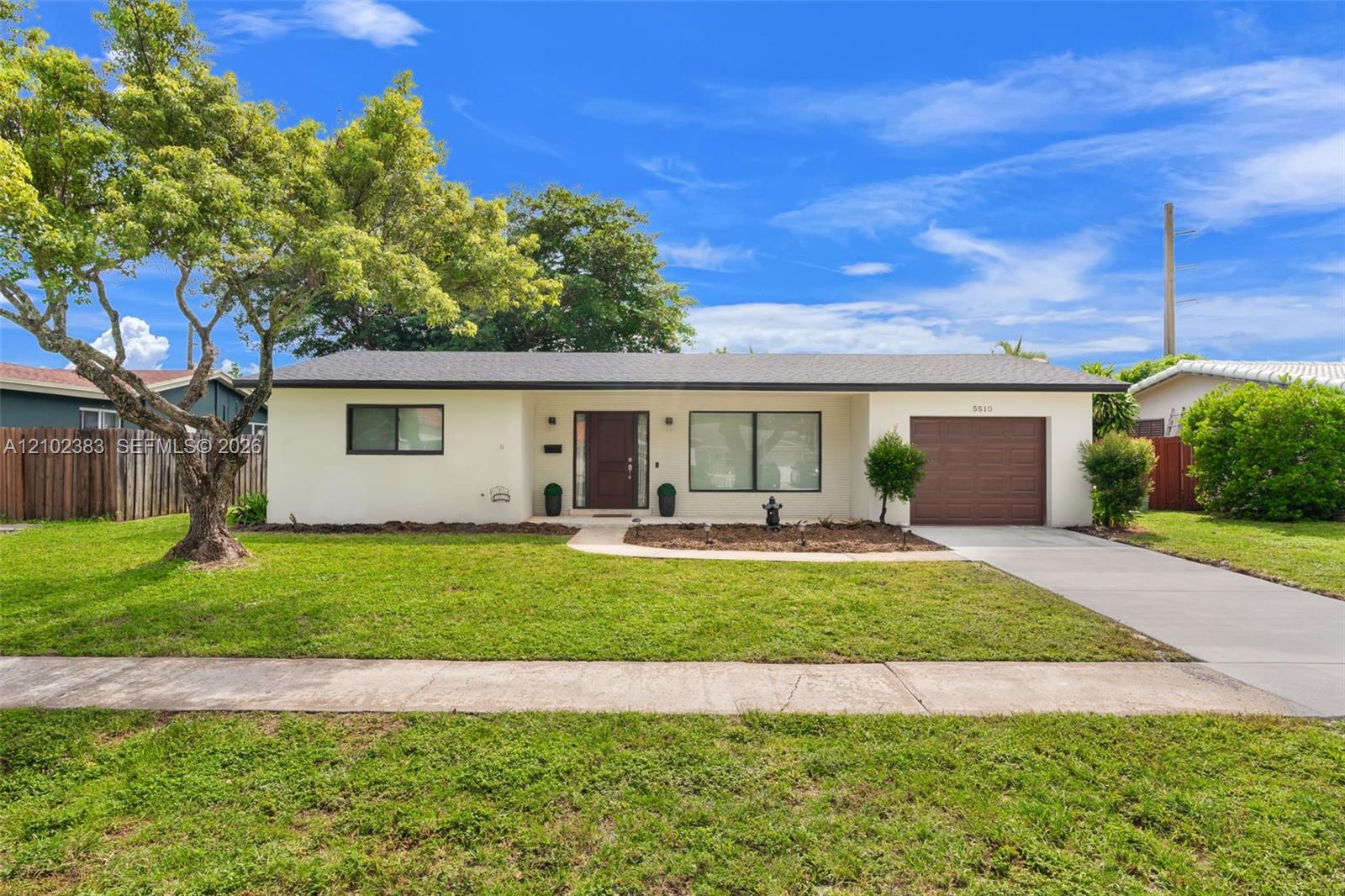 Single-story exterior featuring a light-toned stucco facade, a dark-toned horizontal plank garage door, a covered entryway, and a paved concrete driveway