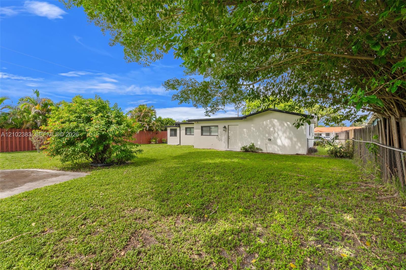 Spacious backyard featuring a manicured lawn, mature trees, concrete patio area, and privacy fencing