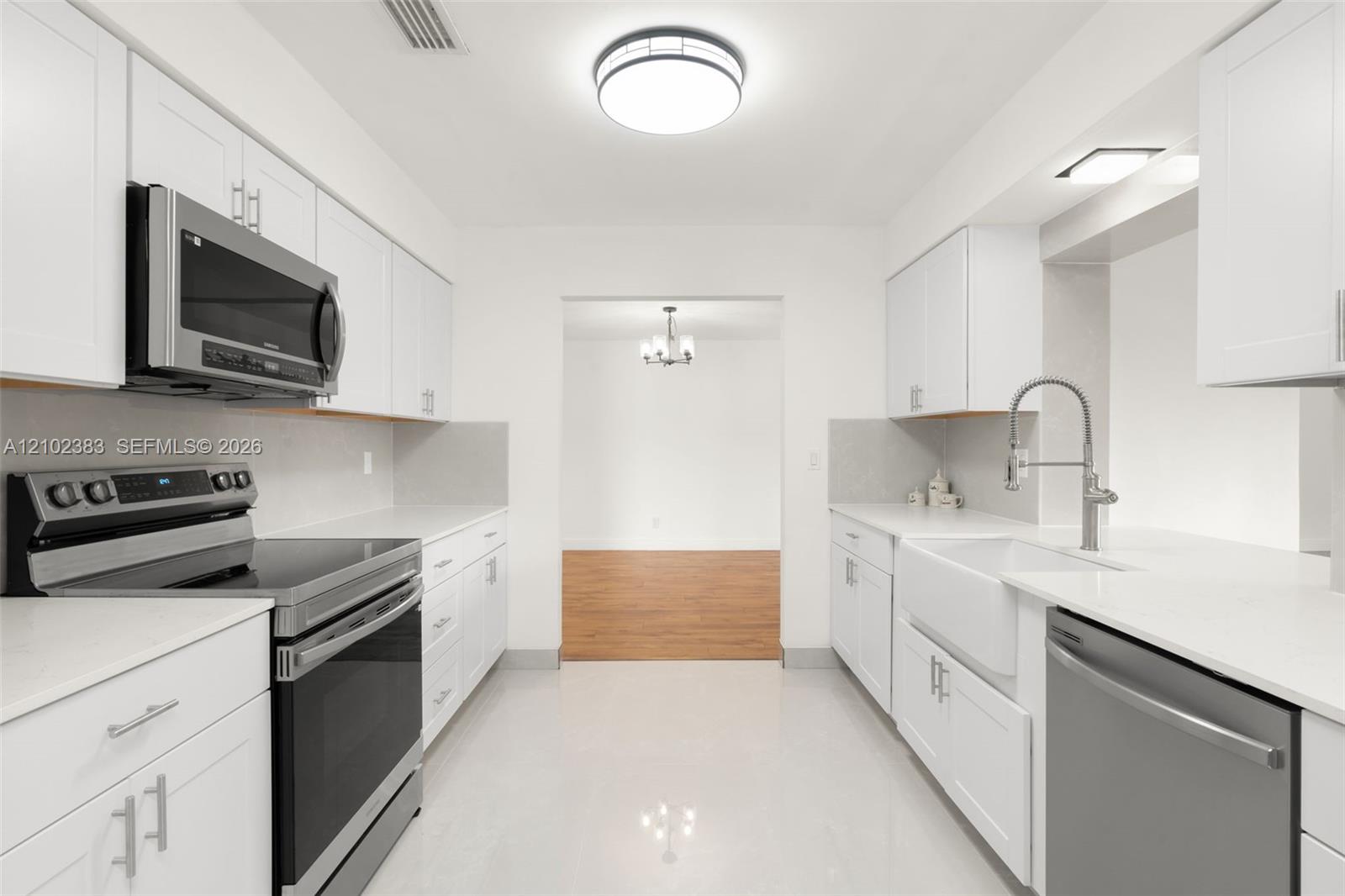 Kitchen featuring white shaker-style cabinetry, solid-surface countertops, a farmhouse-style sink with a pull-down faucet, and stainless steel appliances