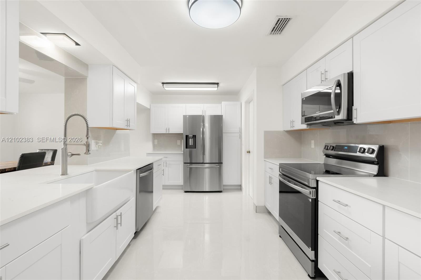 Kitchen featuring white cabinetry, solid-surface countertops, farmhouse sink with arched faucet, stainless steel appliances, and tile flooring