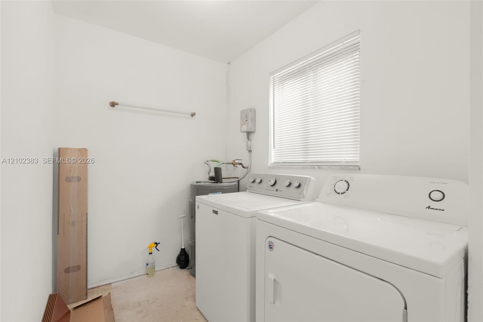 Laundry space featuring white walls, a horizontal window with adjustable blinds, and a built-in wall-mounted hanging rod