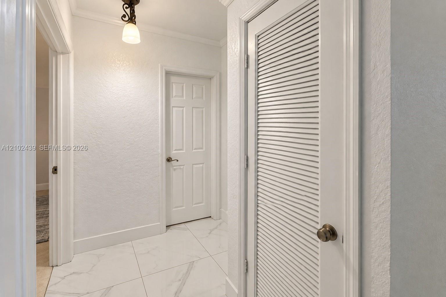 White tile flooring, crown molding, a built-in louvered door, a six-panel door, and a decorative ceiling light fixture