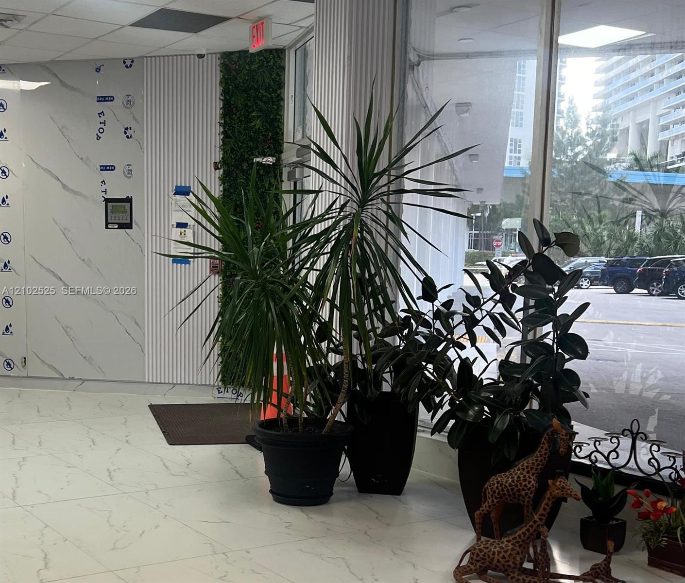 Large-format tile flooring with marble-pattern veining, floor-to-ceiling glass paneling, vertical fluted wall paneling, and an interior green wall feature