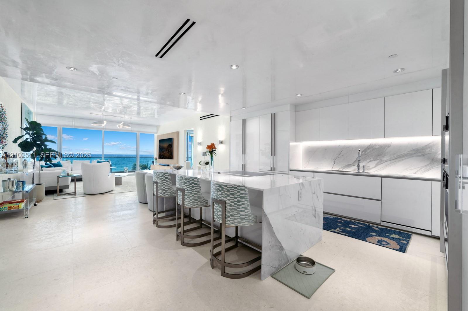 Contemporary kitchen featuring a waterfall-edge island, stone slab backsplash, flat-panel cabinetry, and integrated lighting, set against floor-to-ceiling windows
