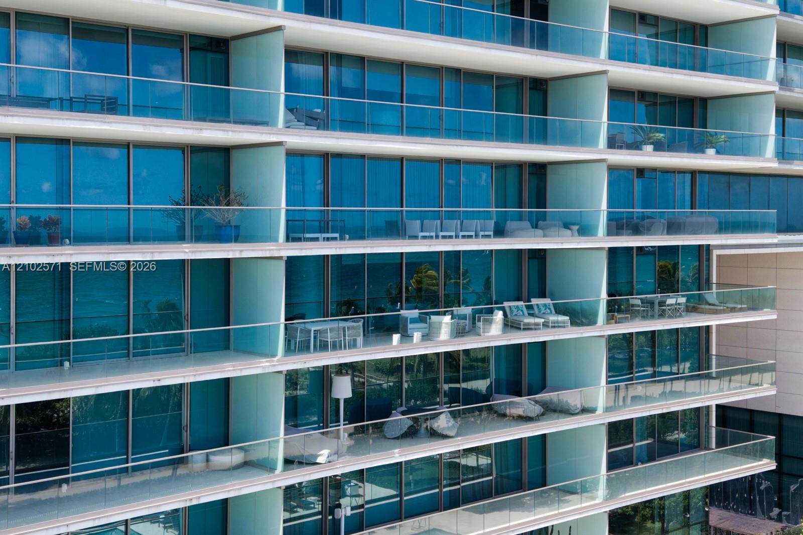 High-rise facade featuring floor-to-ceiling blue-tinted windows, full-width glass-railed balconies, and concrete slab terrace dividers