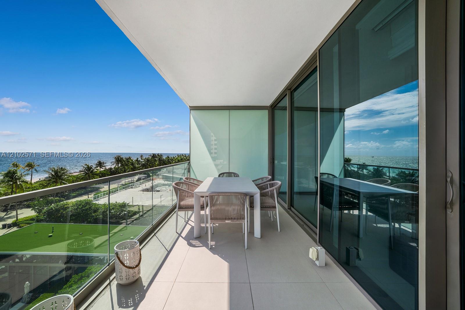 Covered balcony featuring expansive tile flooring, a glass-panel railing, and floor-to-ceiling sliding glass doors