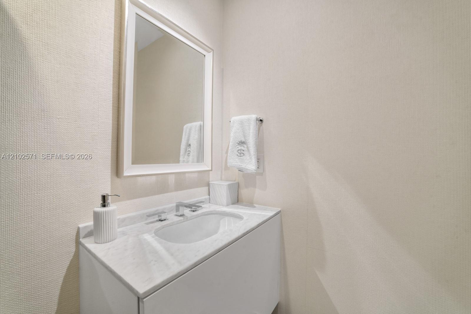 White vanity featuring a stone countertop with an integrated basin, a wall-mounted rectangular mirror, and a chrome single-lever faucet