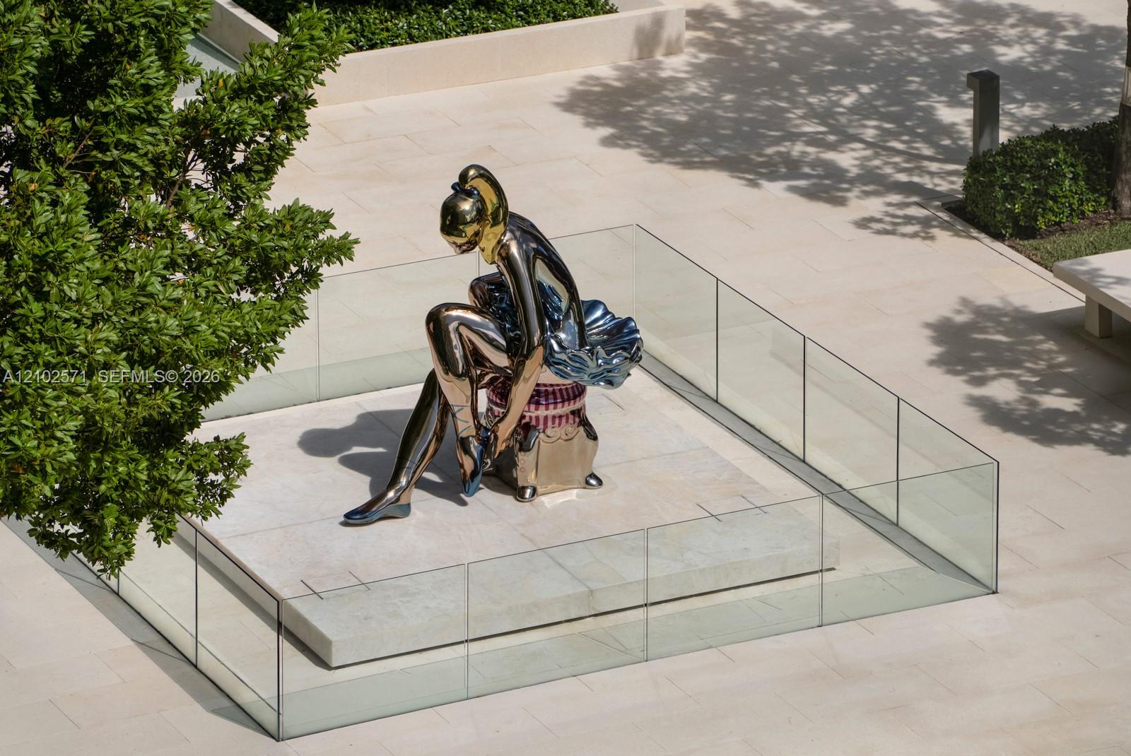 Communal courtyard featuring large-scale metallic sculpture, raised stone pedestal, perimeter glass railing, and smooth stone paving