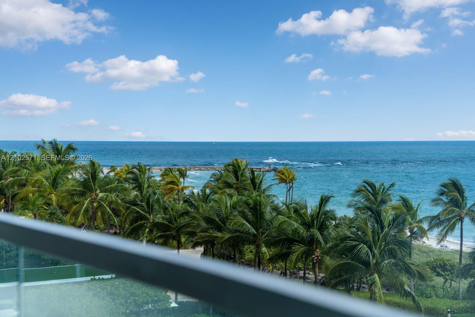 Balcony featuring a glass railing and direct ocean exposure with mature palm trees