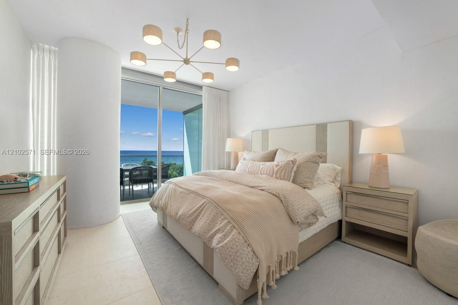 Floor-to-ceiling glass sliding doors with access to an exterior terrace, neutral stone-finish flooring, and a contemporary multi-arm chandelier