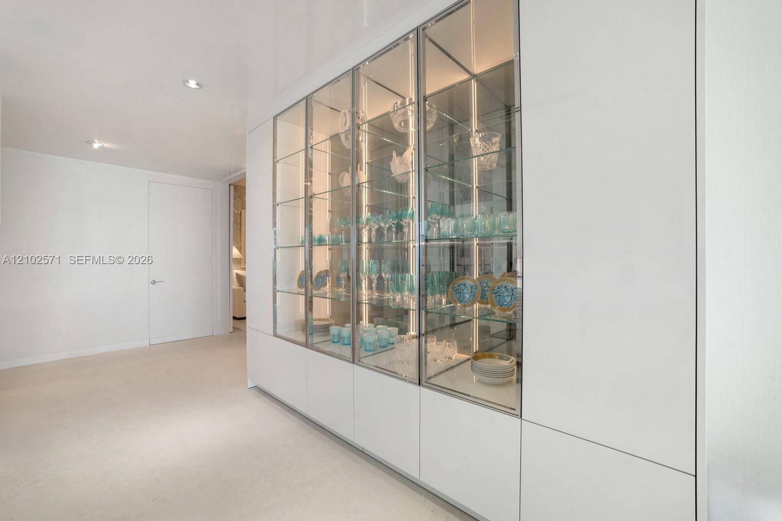 Built-in floor-to-ceiling cabinetry featuring white panel doors and glass-fronted display sections with integrated interior lighting