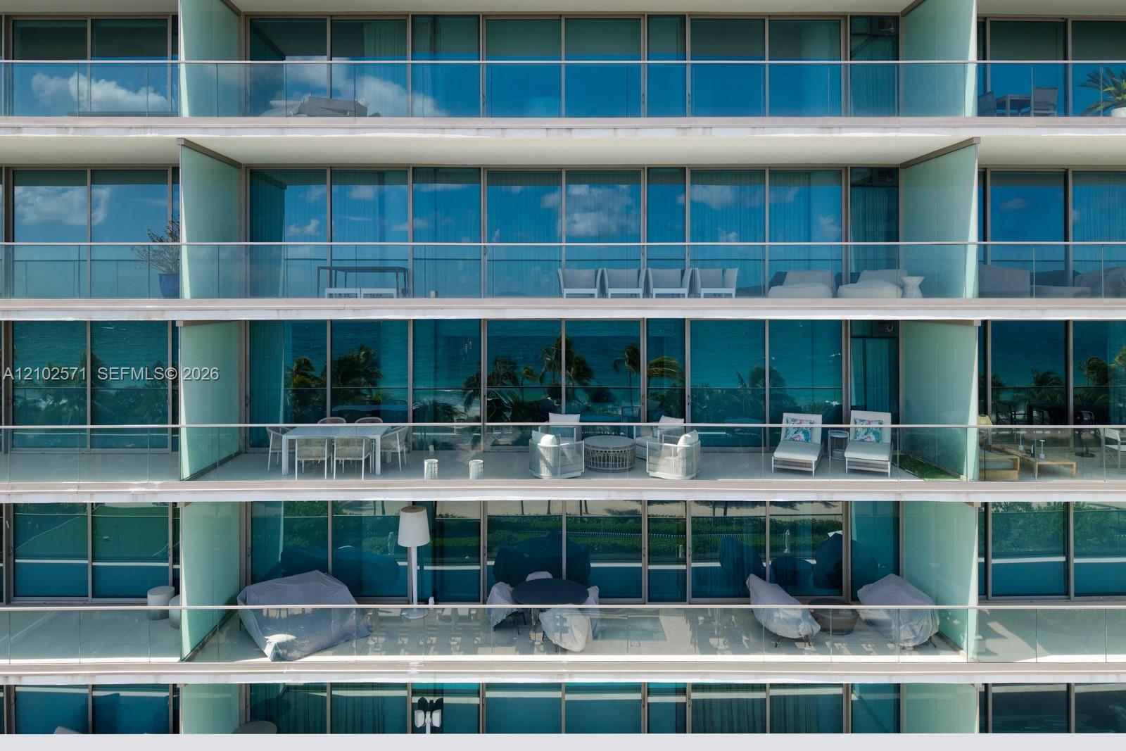 Multi-level residential exterior featuring floor-to-ceiling glass paneling, horizontal cantilevered balconies, and glass-railing balustrades