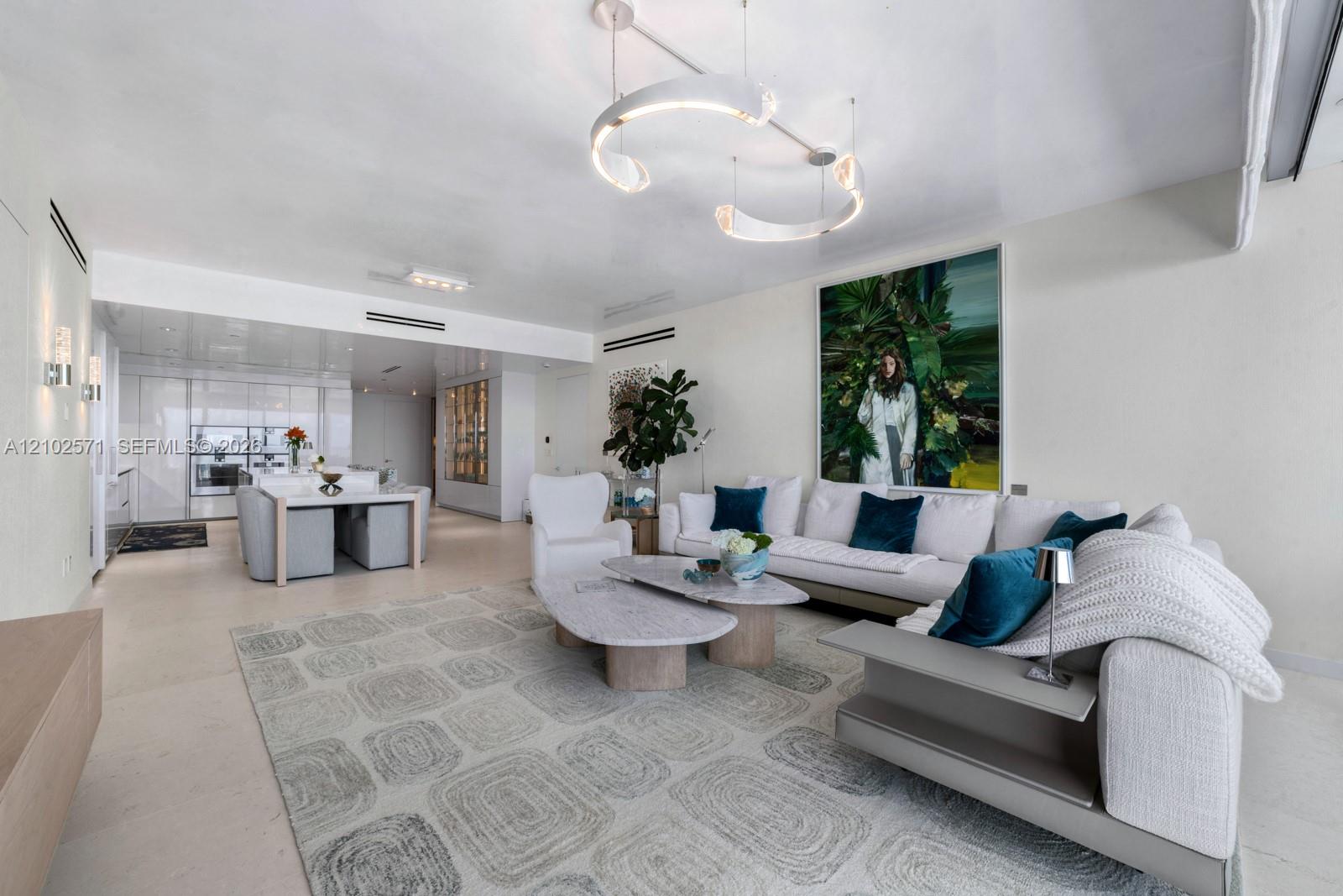 Open-concept main living area featuring stone-finish flooring, recessed linear lighting, a contemporary curved pendant chandelier, and sleek built-in cabinetry
