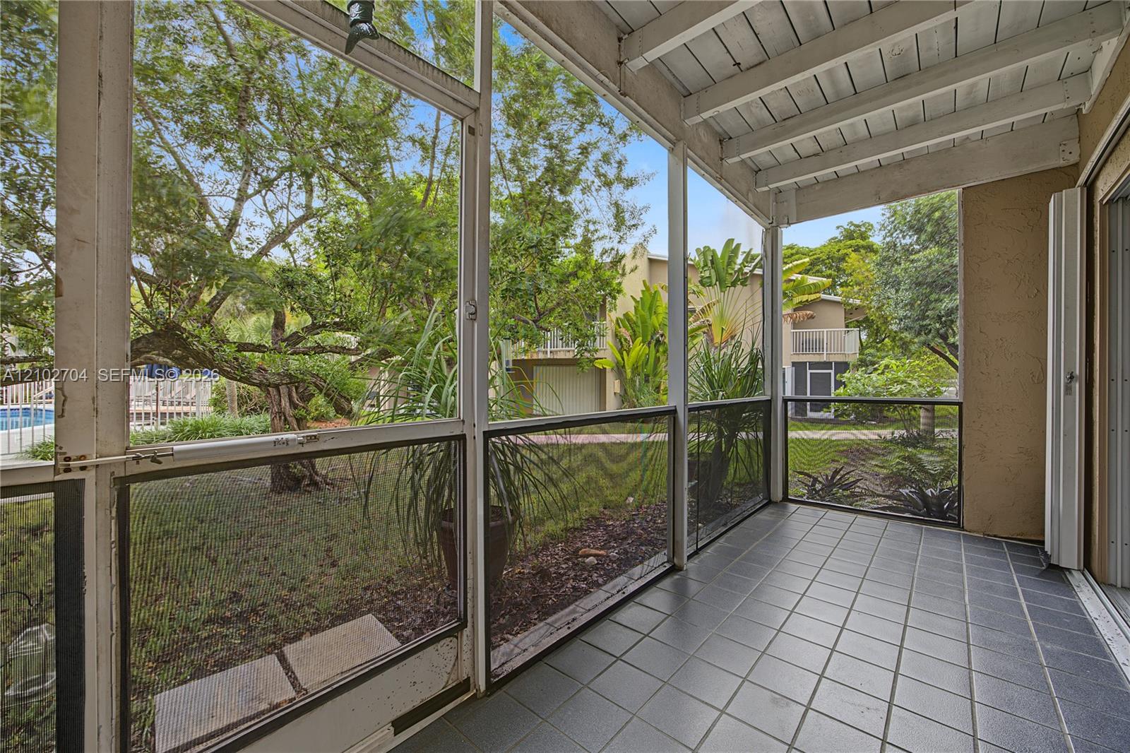 Screened-in porch featuring tile flooring, exposed beamed ceiling, and floor-to-ceiling screen panels