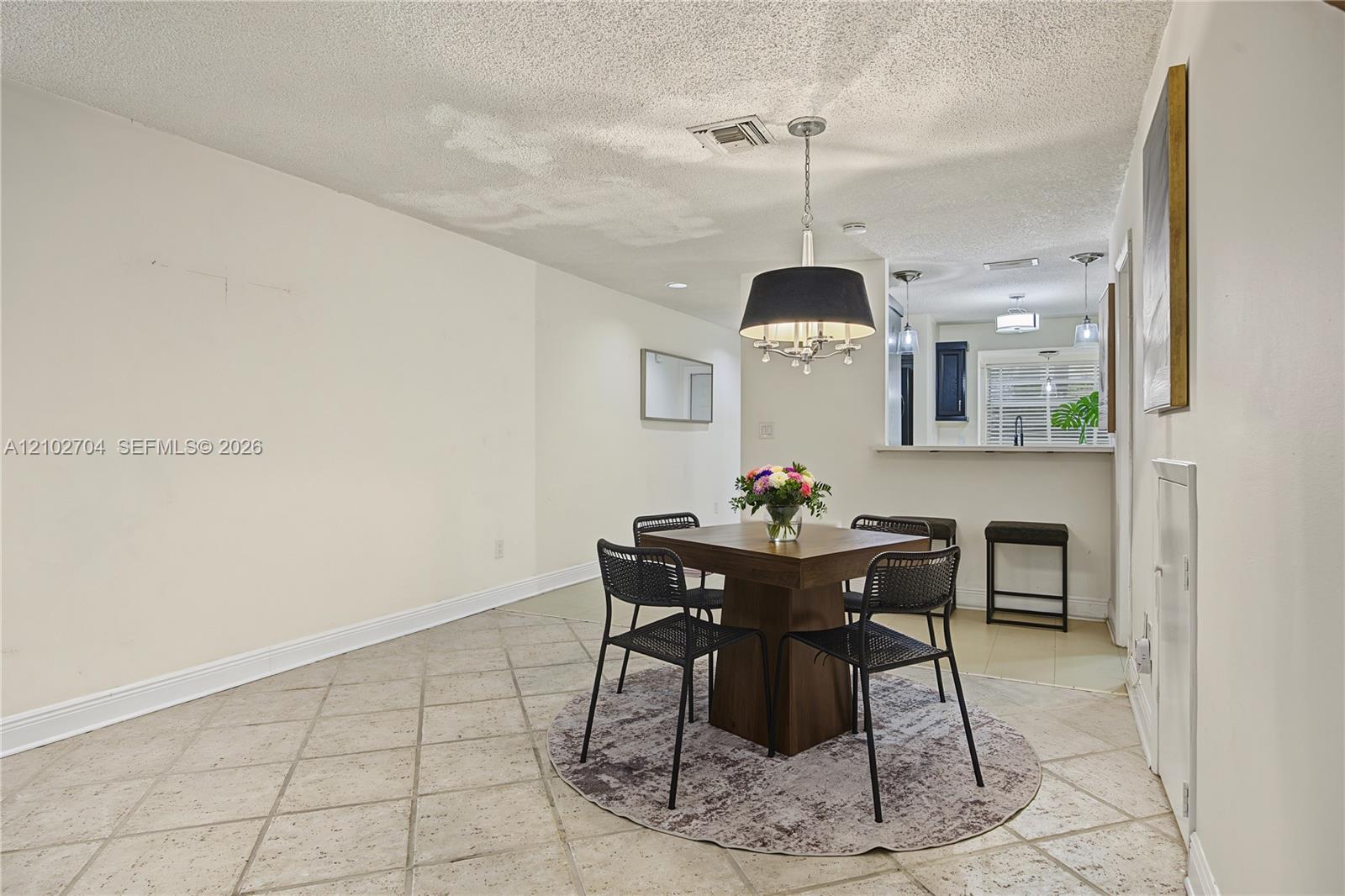 Dining area featuring ceramic tile flooring, a structured drum pendant light fixture, and a pass-through breakfast bar