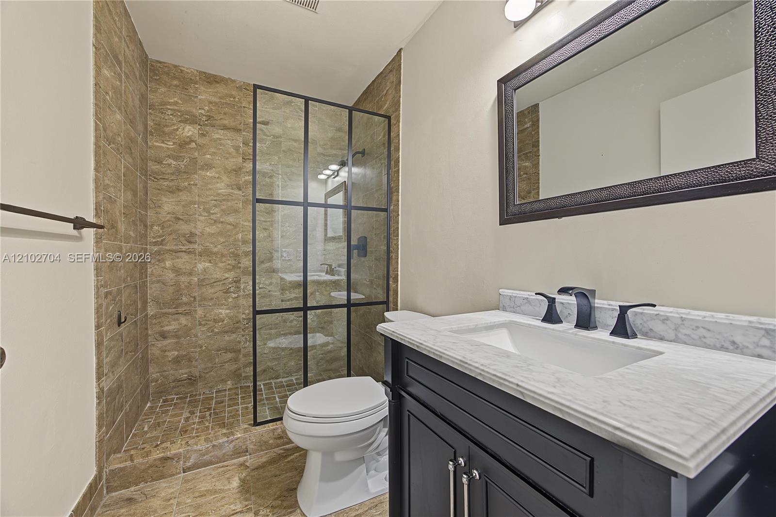 Bathroom featuring a stone-tile walk-in shower with a black-frame glass enclosure, dark vanity cabinet, stone countertop with an integrated basin, and black faucet fixtures