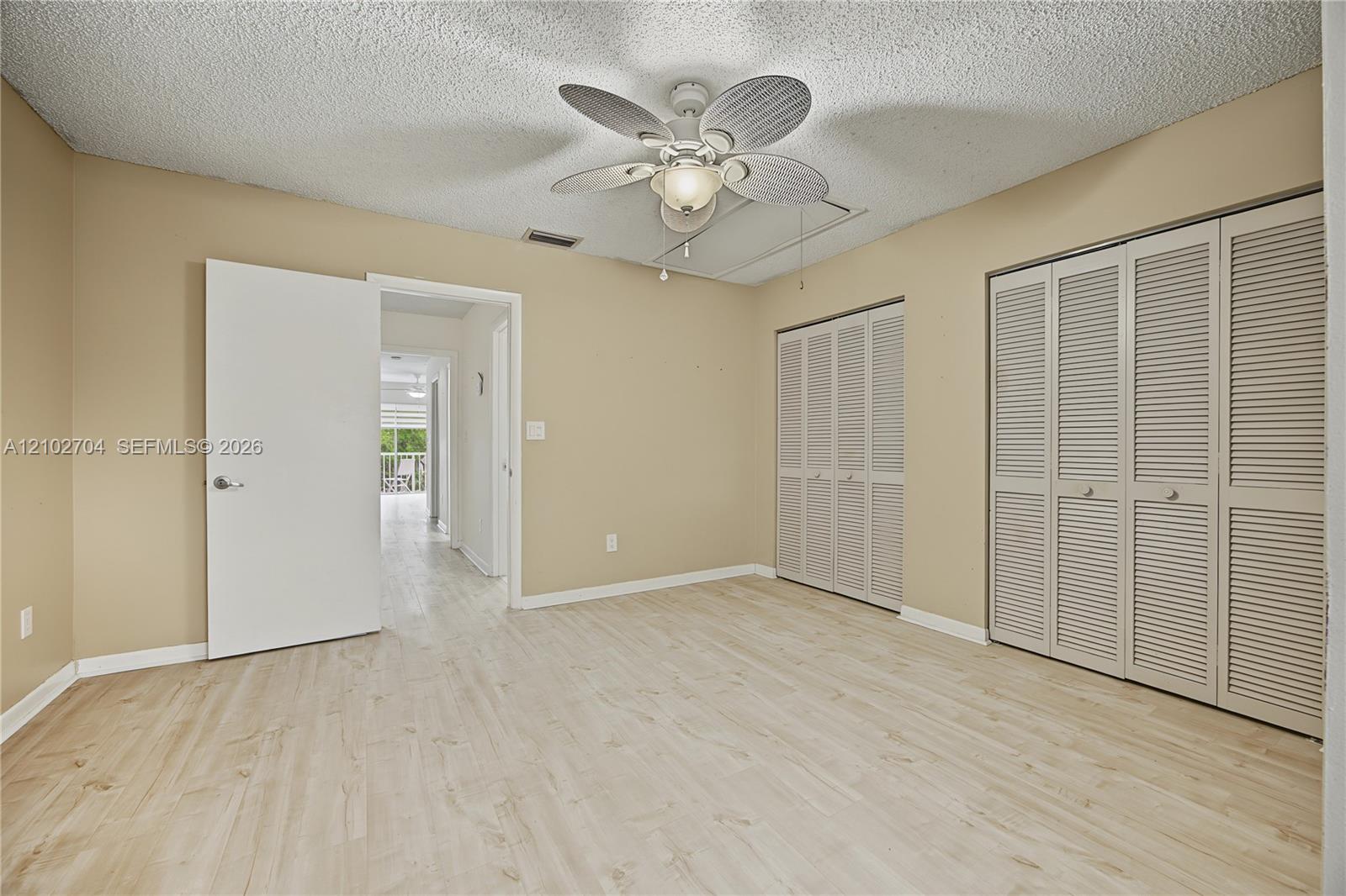 Room featuring wood-finish flooring, a ceiling fan with integrated lighting, and dual louvered-door closets