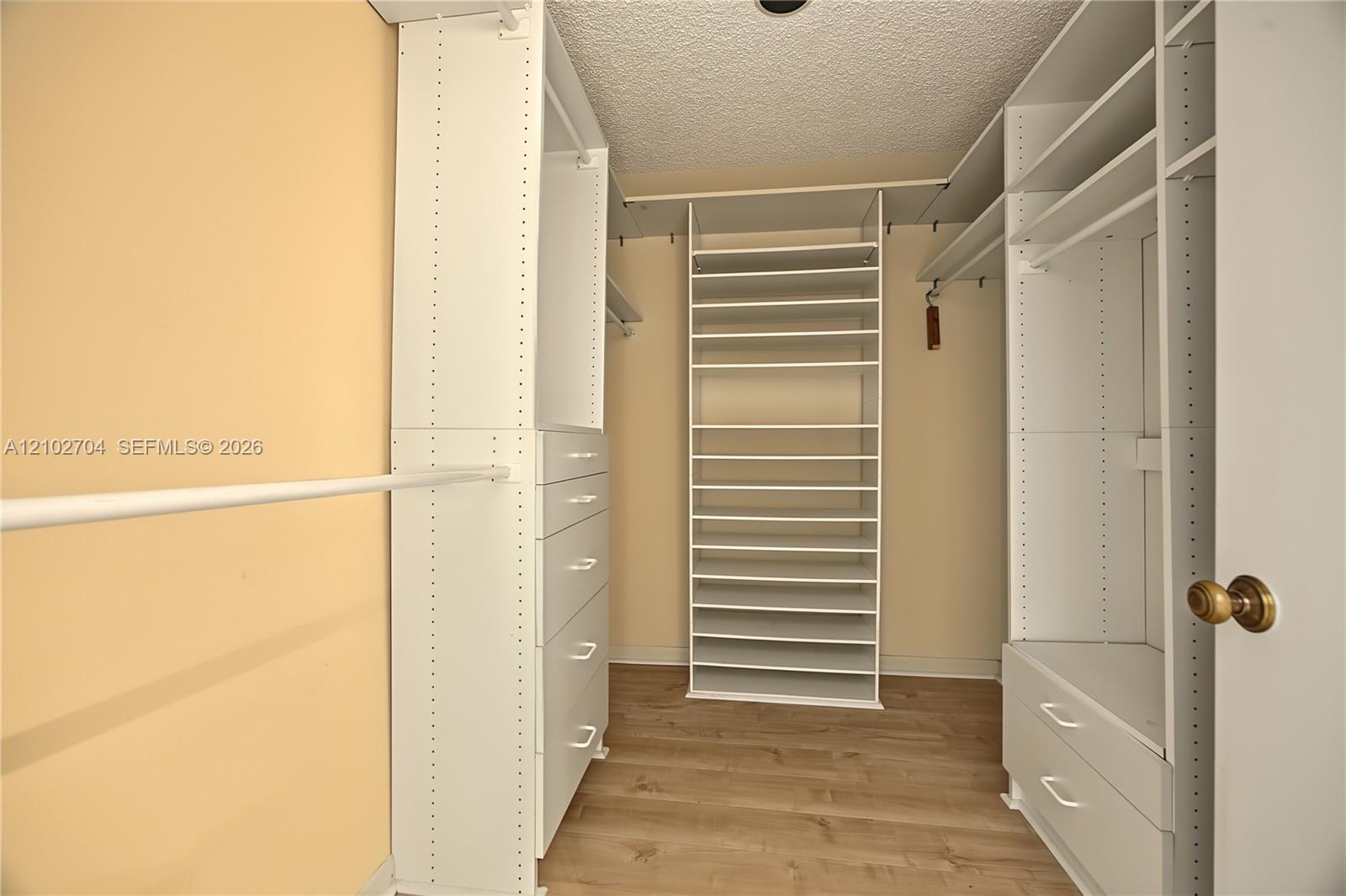 Walk-in closet featuring white built-in shelving, modular organizers, integrated storage drawers, and wood-finish flooring