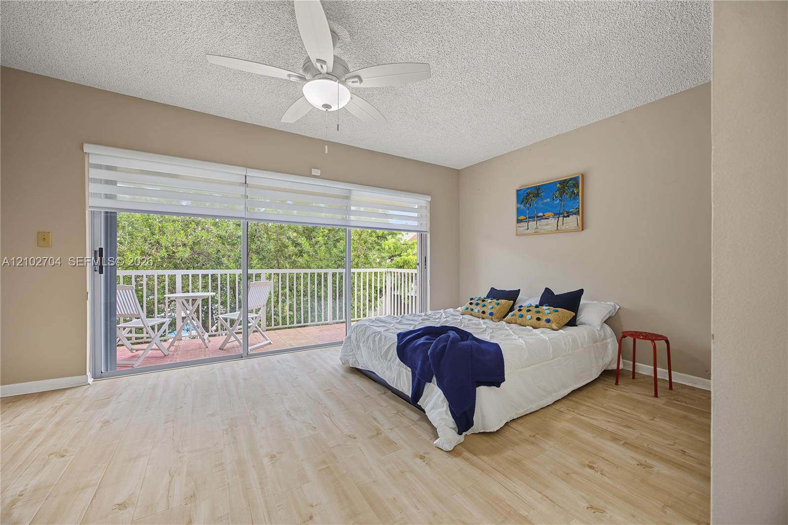 Wood-finish flooring, ceiling fan with integrated lighting, and floor-to-ceiling sliding glass doors opening to a covered balcony with a white railing
