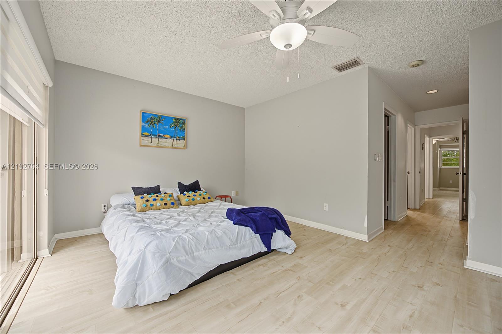 Light-toned wood-finish flooring, neutral wall palette, ceiling fan with integrated lighting, and glass sliding door access to exterior space