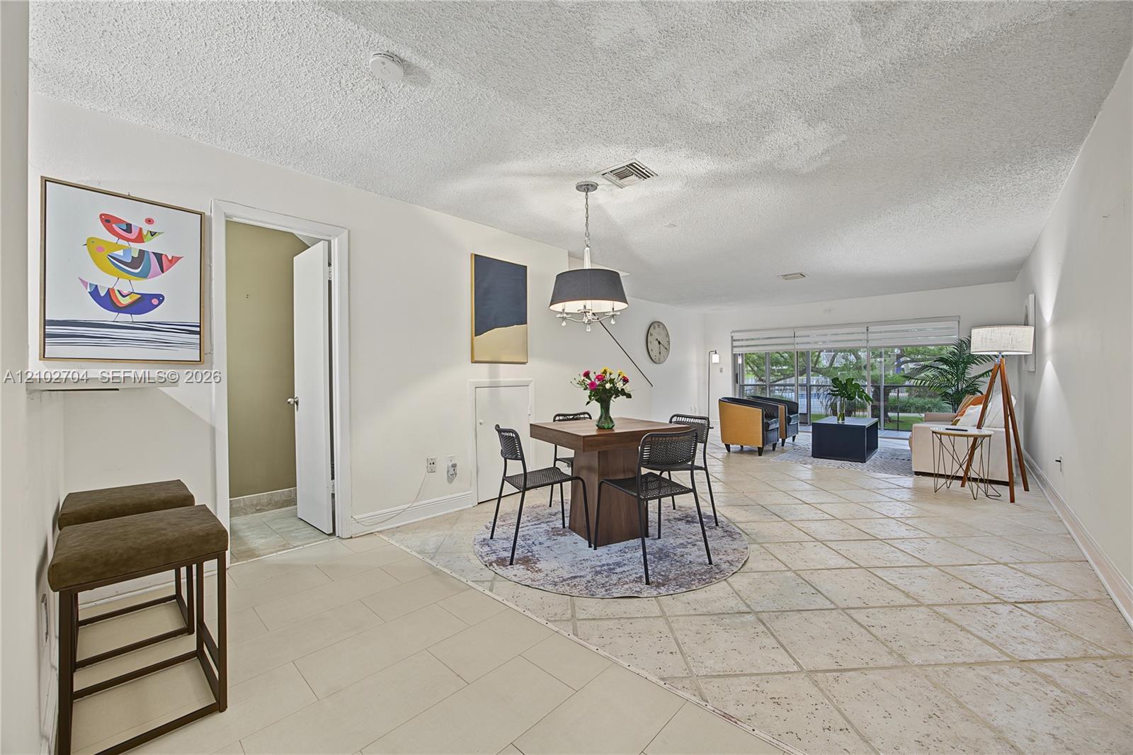 Open-concept interior featuring large-format ceramic tile flooring, a structured drum pendant light, and sliding glass doors with horizontal blinds