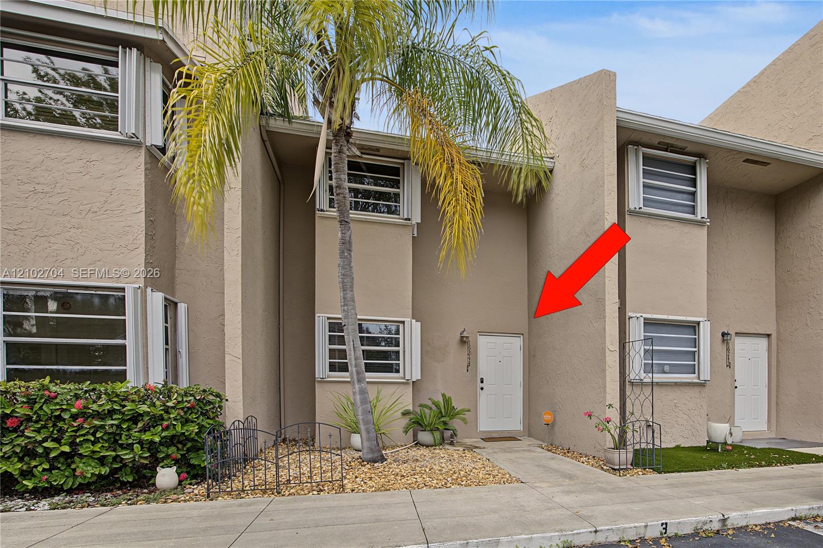 Stucco exterior featuring horizontal louvered shutters, decorative metal fencing, and a private entrance with wall-mounted lighting