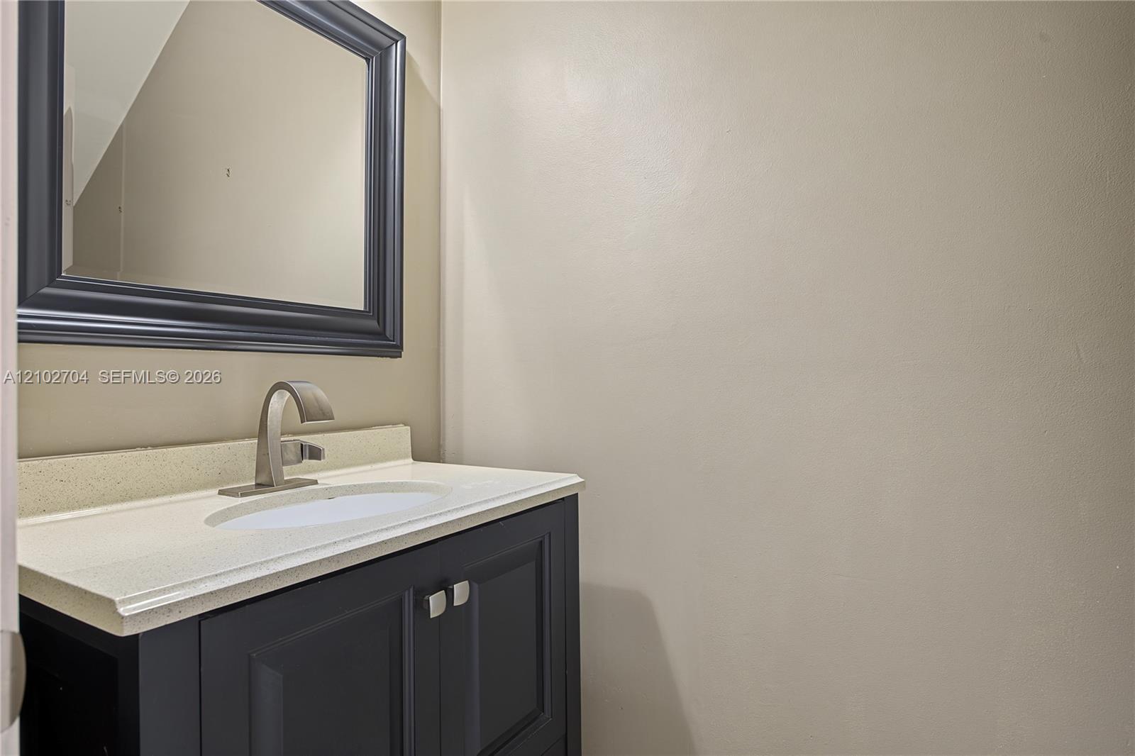 Vanity featuring dark-toned cabinetry, a light-colored solid surface countertop, an undermount sink, a high-arc faucet, and a coordinating dark-framed mirror
