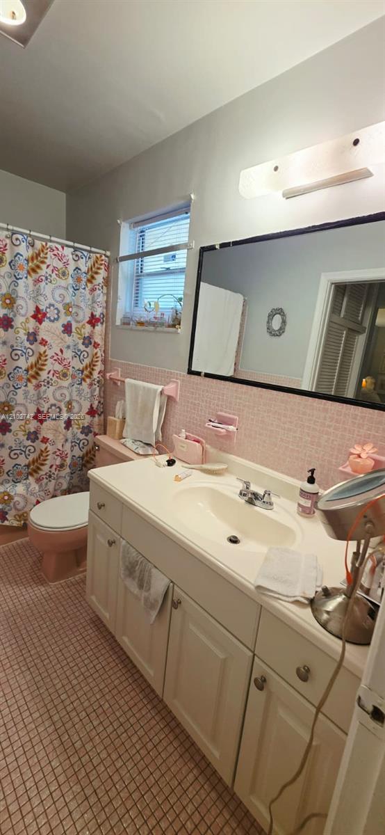 Bathroom featuring white cabinetry, integrated sink, large wall-mounted mirror, mosaic-tiled walls, and a multi-light fixture