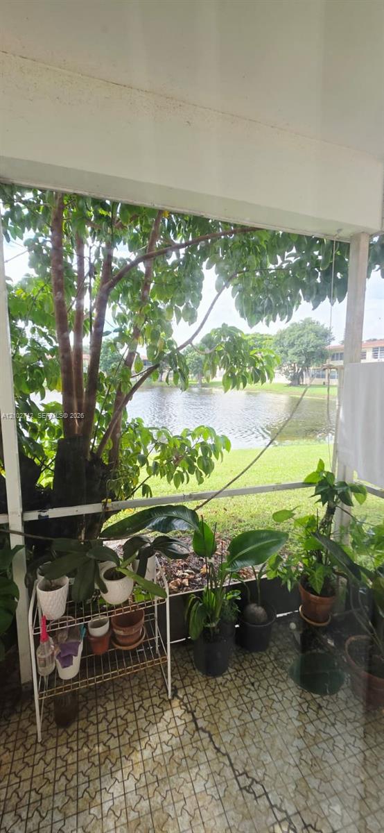 Screened lanai featuring tiled flooring, structural support pillars, and direct exterior access to a pond