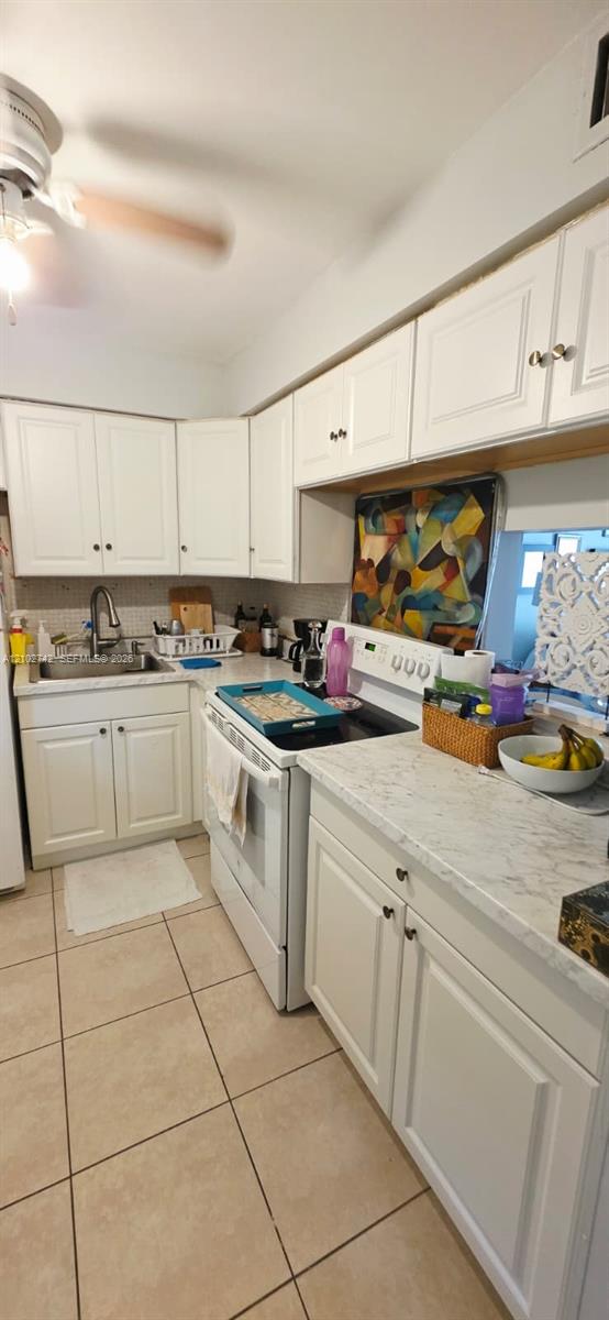 Kitchen featuring white shaker-style cabinetry, stone-patterned countertops, stainless steel sink with a high-arch faucet, integrated ceiling fan, and tile flooring