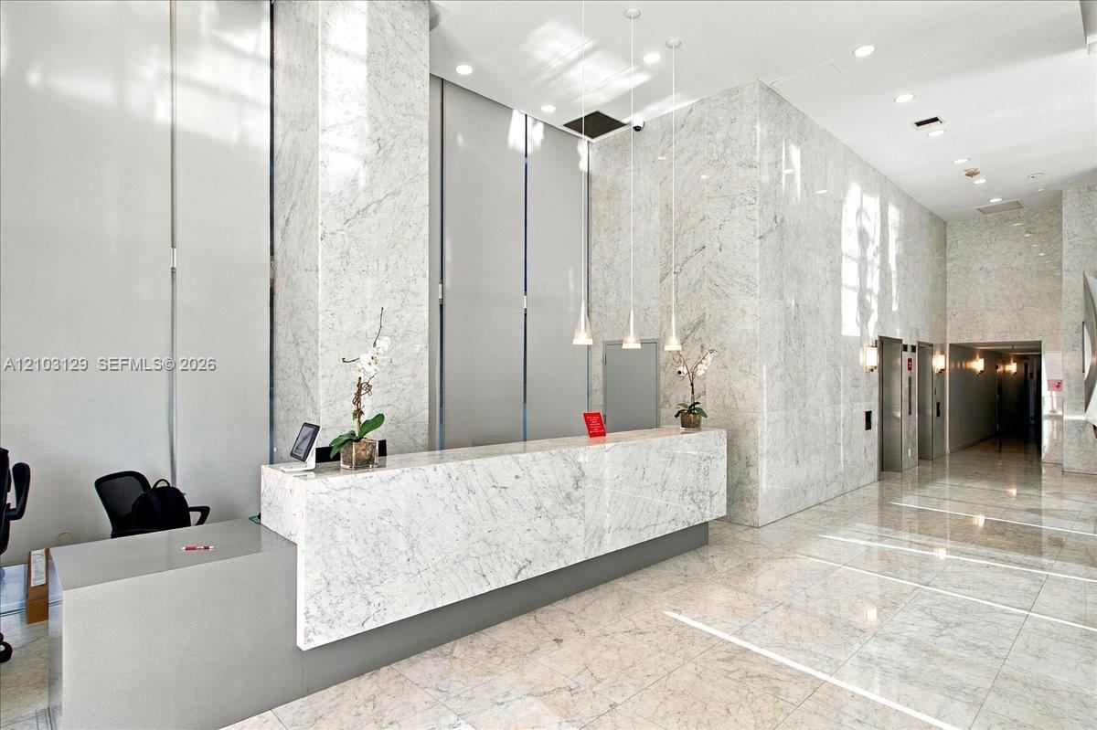 High-ceilinged lobby featuring full-height stone wall cladding, polished stone flooring, a custom stone reception desk, and minimalist pendant lighting