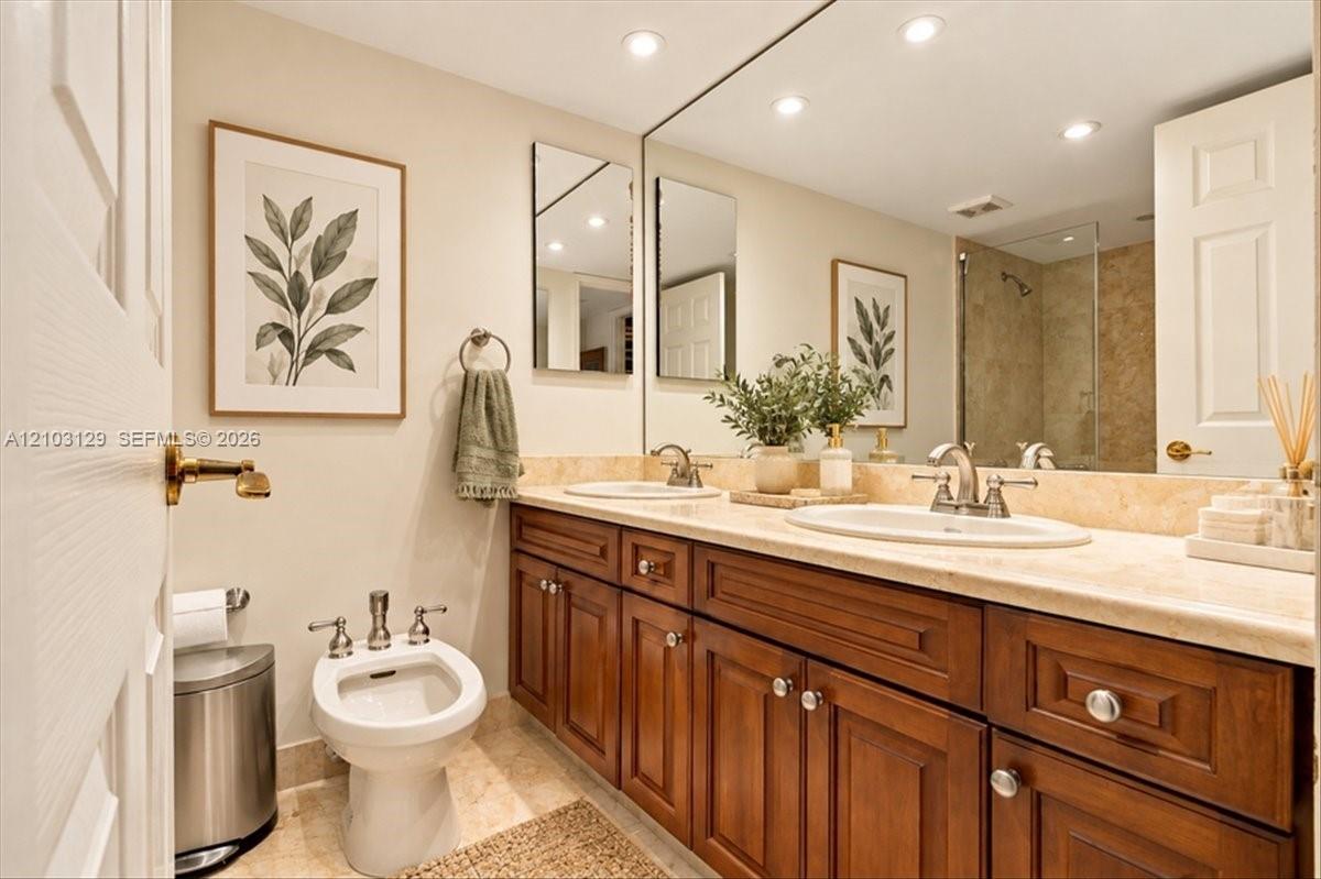 Double vanity with stone countertop, undermount sinks, wood-finish cabinetry, full-width wall mirror, and porcelain bidet