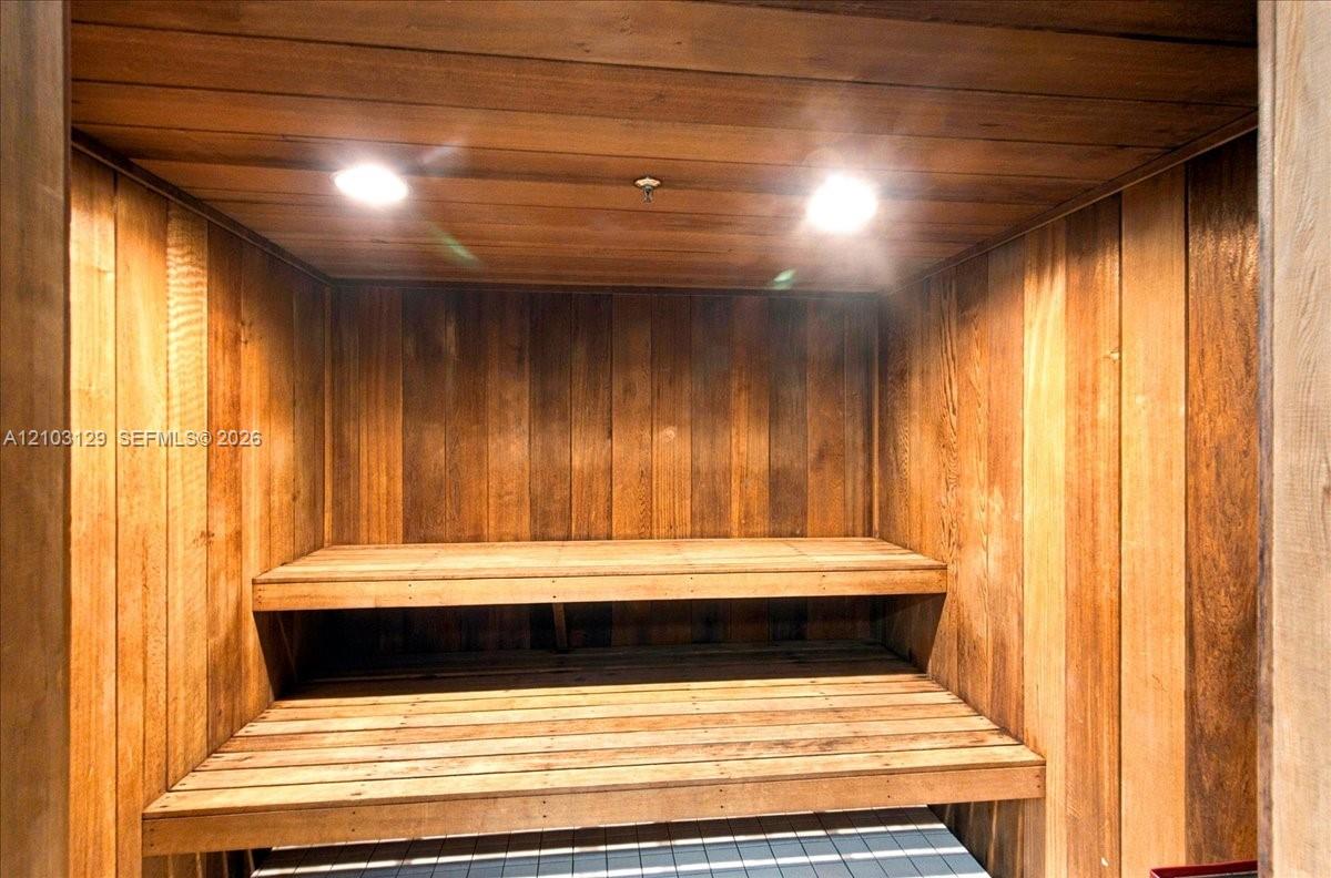 Sauna featuring natural wood wall paneling, tiered built-in wood bench seating, and recessed ceiling lighting