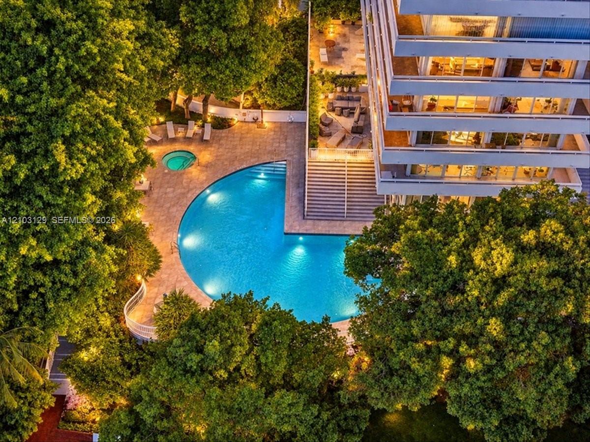 Multi-level building exterior featuring a crescent-shaped swimming pool, built-in spa, stone-finish pool deck, and mature landscaping