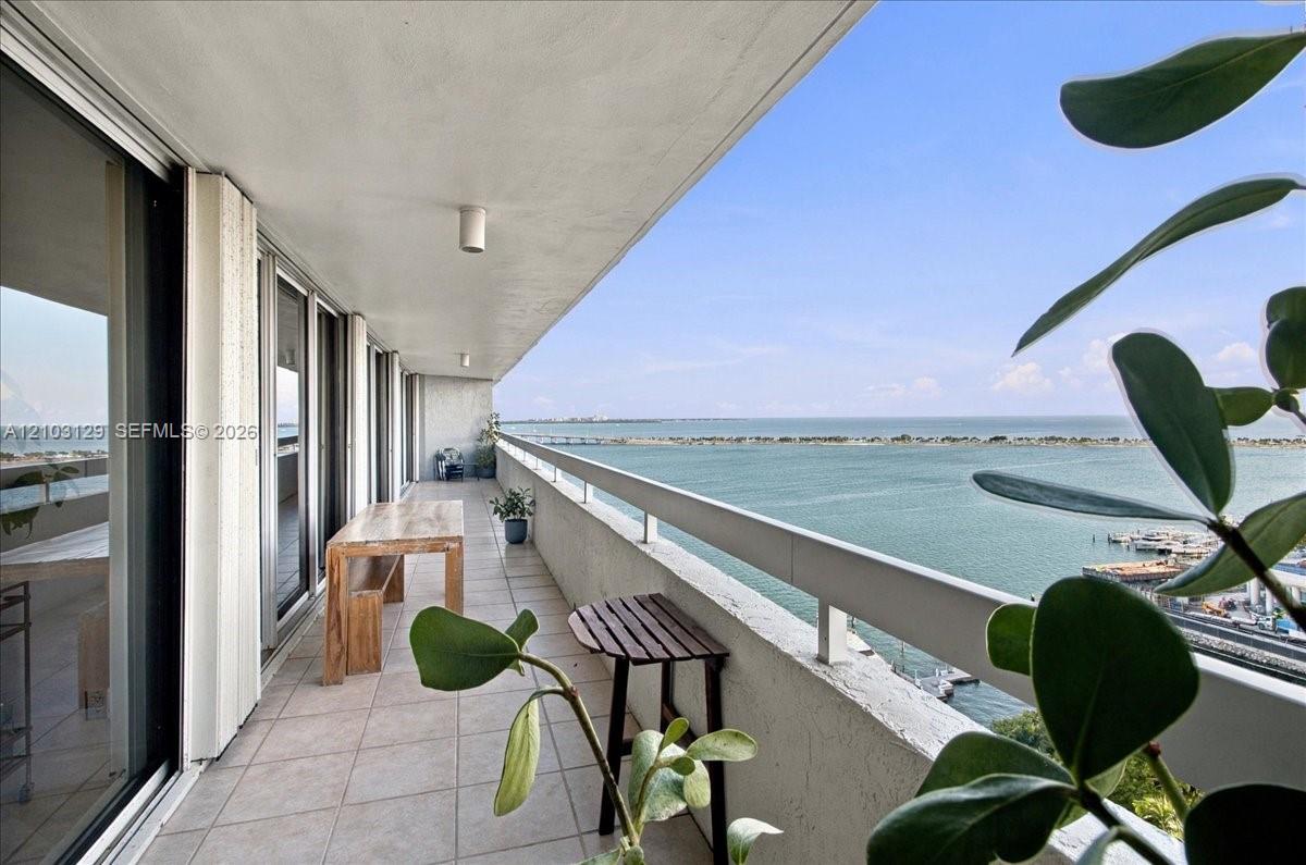 Expansive covered balcony featuring tile flooring, a concrete ceiling with integrated lighting, and a metal railing overlooking the water